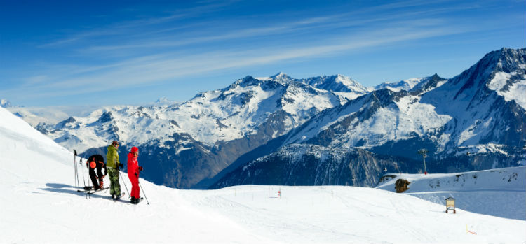 three skiers on top of a mountain peak.