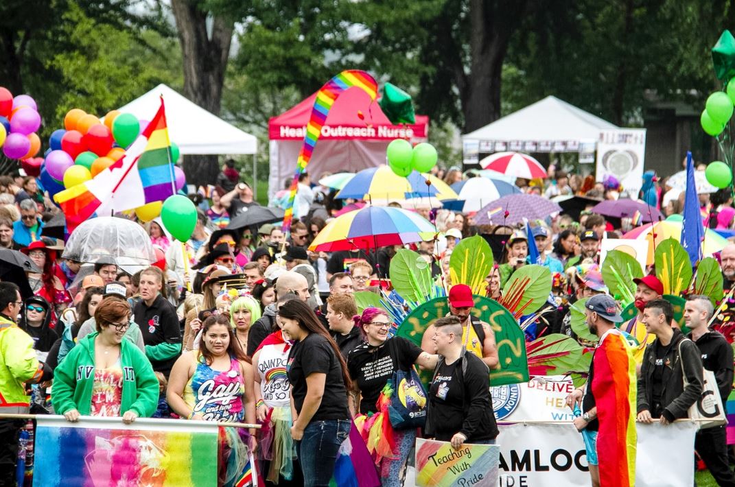 Kamloops Pride event with a group of people with multi-coloured flags. 